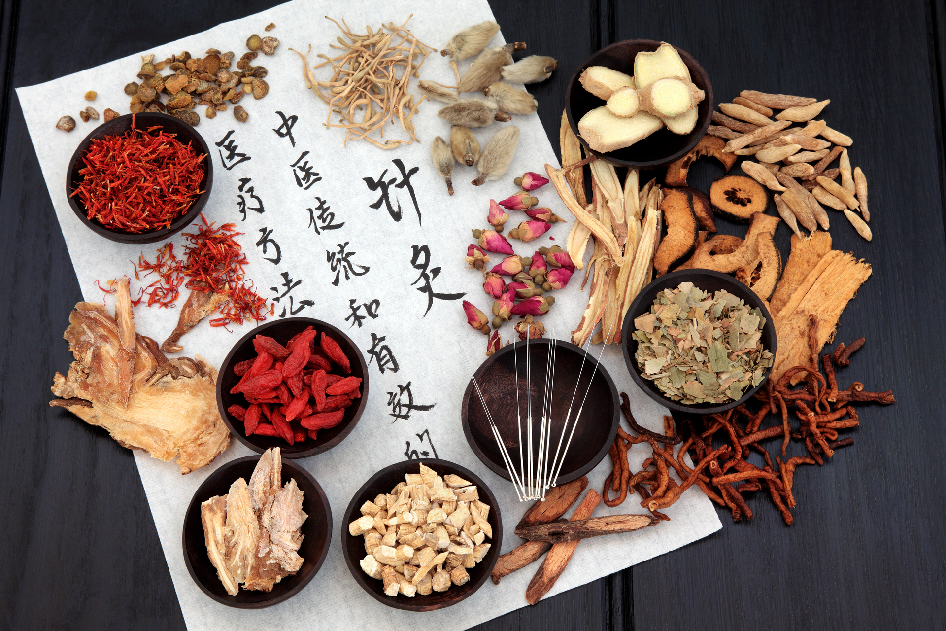 Na tym obrazku widzimy różnorodne zioła stosowane w medycynie chińskiej. Na stole ułożone są suszone rośliny, takie jak goździki, żeń-szeń i mięta, które są znane ze swoich właściwości leczniczych. Ich naturalne kolory i intensywny aromat wzbudzają zainteresowanie. Możemy dostrzec różnorodność kształtów i tekstur ziół, co świadczy o ich różnorodnych właściwościach i zastosowaniach.